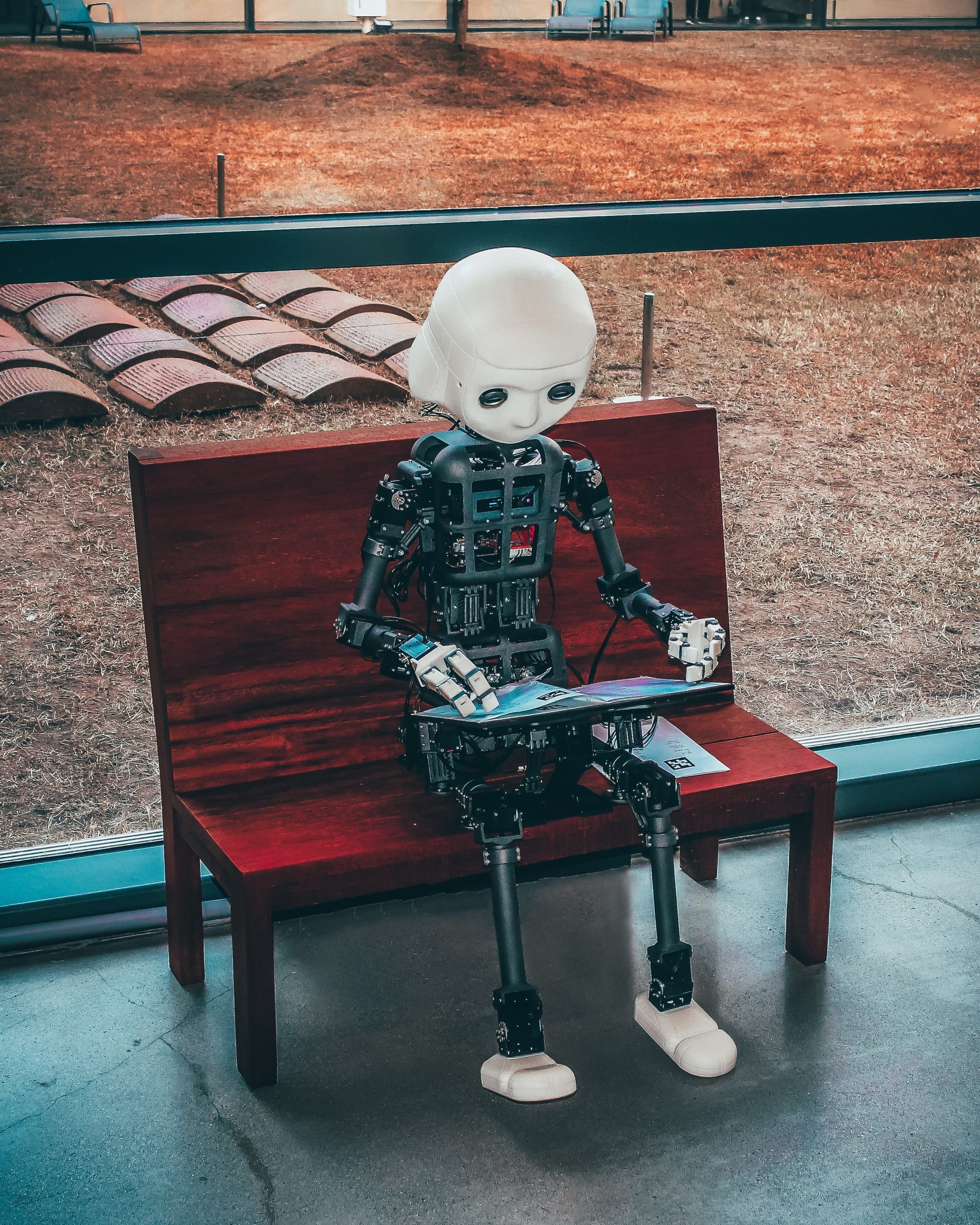 A robot reading a magazine on a park bench