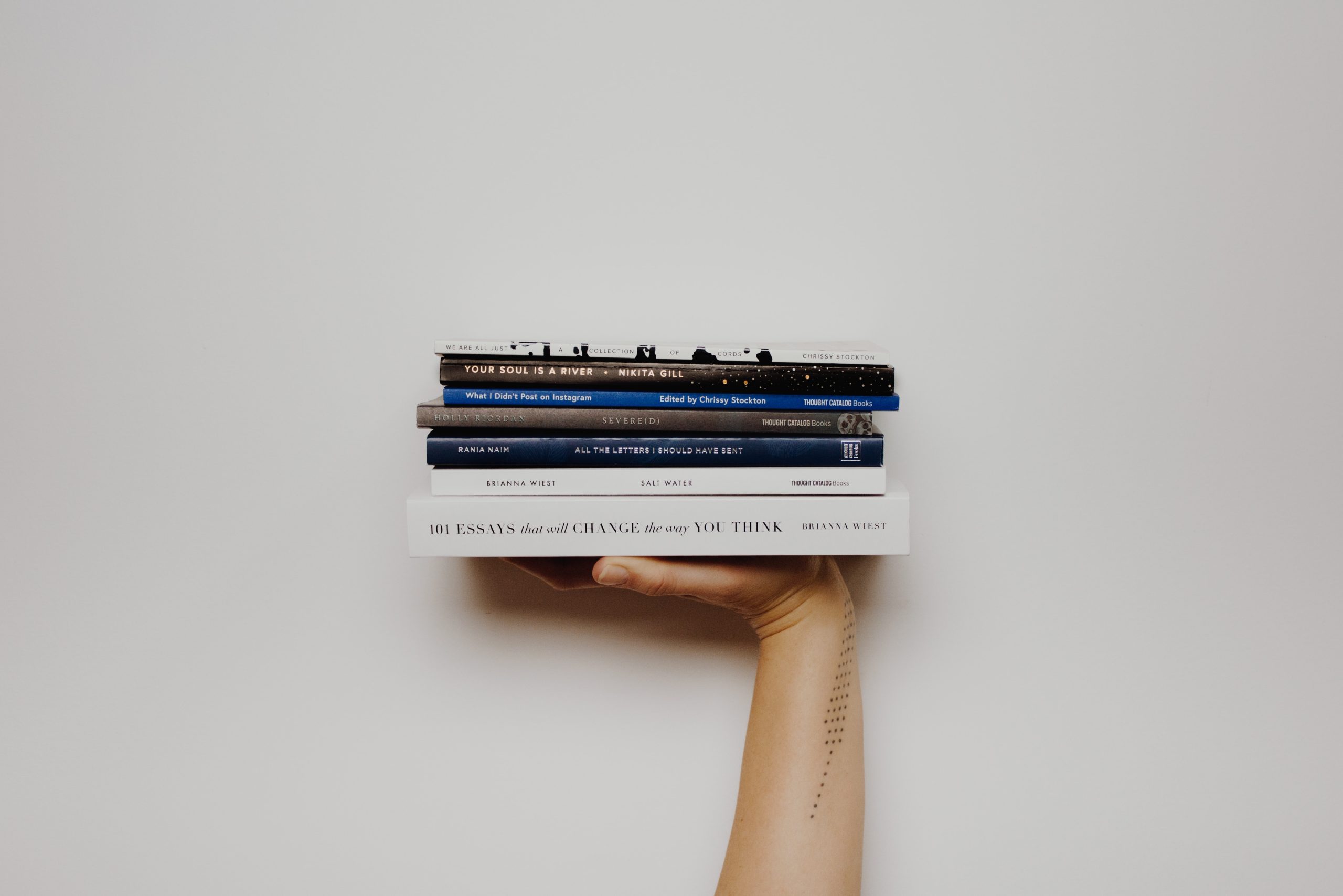 A hand holding up a small stack of books with two white books on the bottom and some darker books on top.